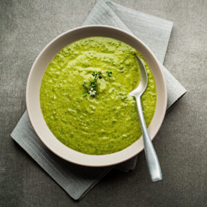 Vellutata verde cremosa servita in ciotola beige con cucchiaio