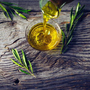 Olio extravergine d’oliva versato in una ciotola di vetro con rametti di ulivo su tavola rustica